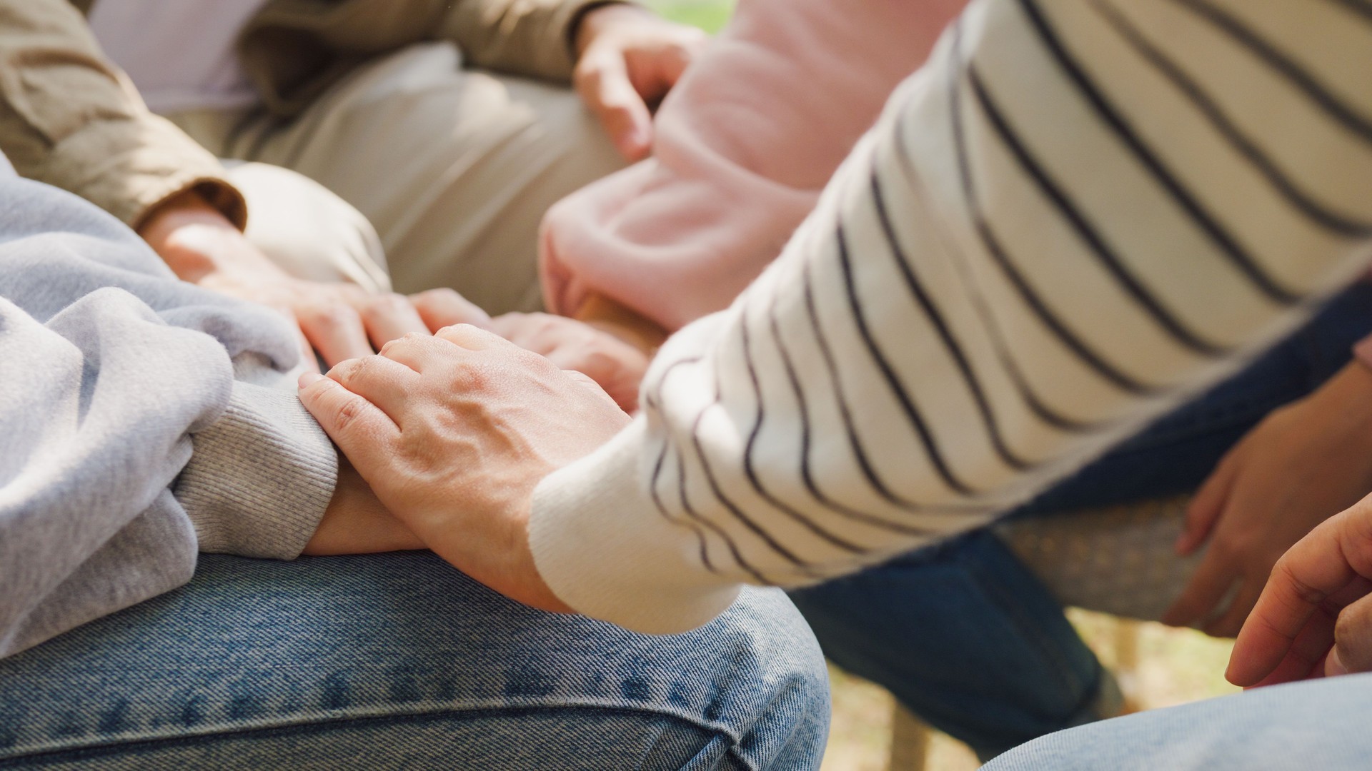 Close-up of diverse multiracial men and women group sit in circle hold hands together hope for help people in park. Support and understand at psychological therapy session, PTSD Mental health.